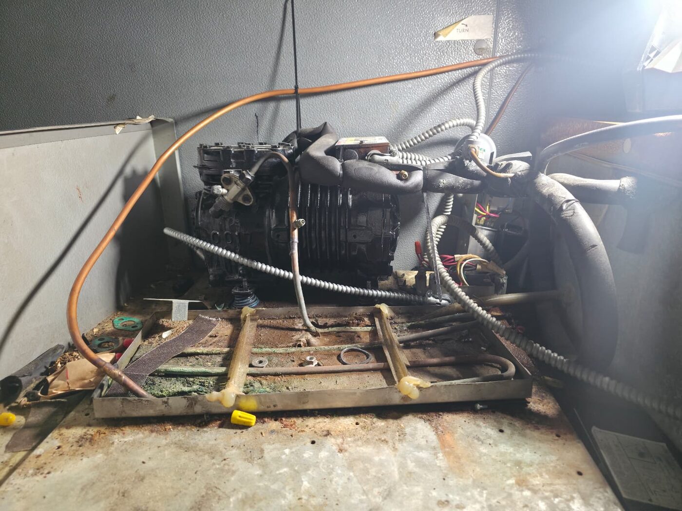 Exposed semi-hermetic refrigeration compressor with copper suction lines undergoing repair on a rusted equipment base