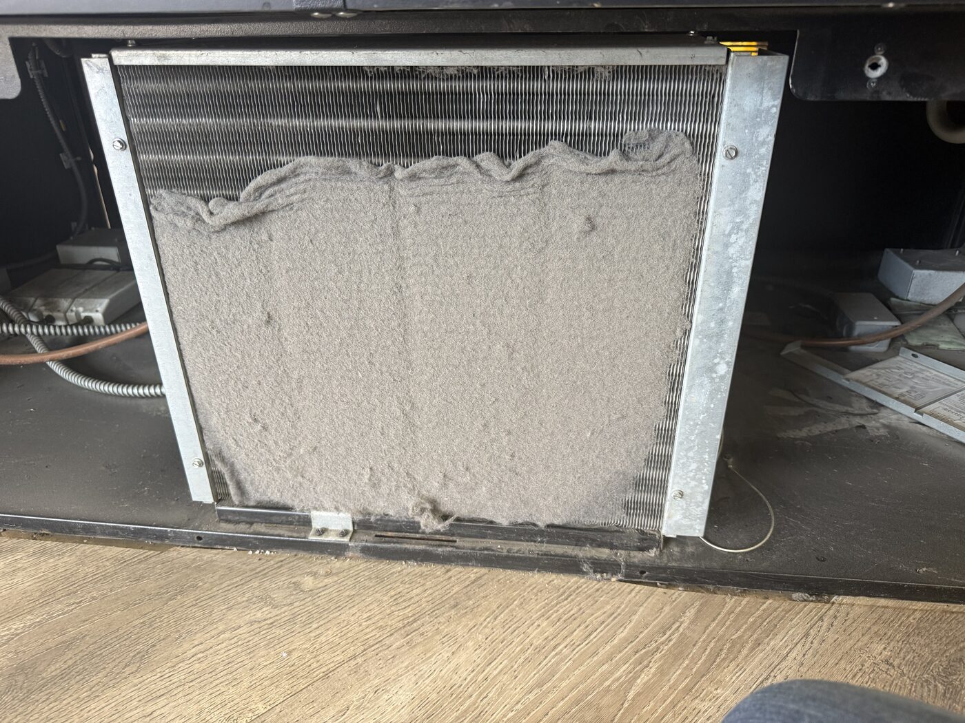 Severely clogged refrigeration condenser coil packed with lint and dust before cleaning
