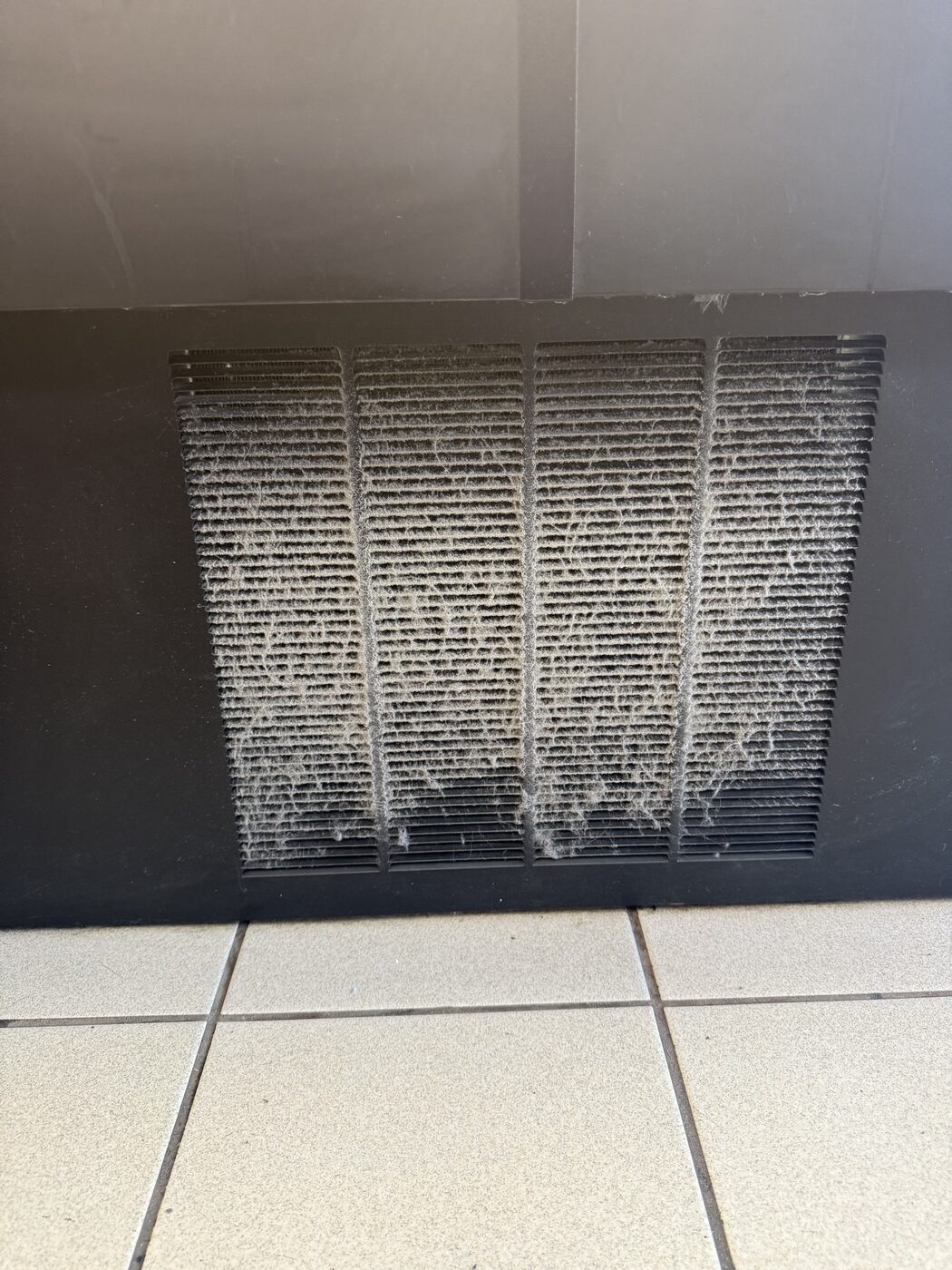 Dusty condenser grille on a commercial refrigerator with lint clogging the fins