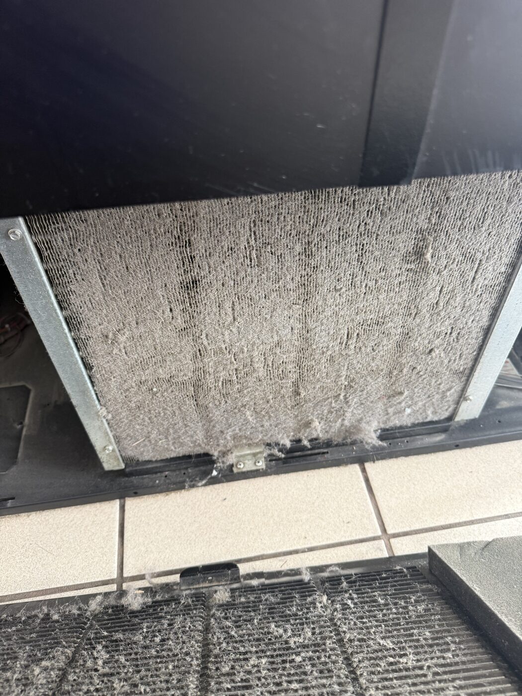 Heavily clogged condenser air filter caked with dust and lint on a commercial refrigerator