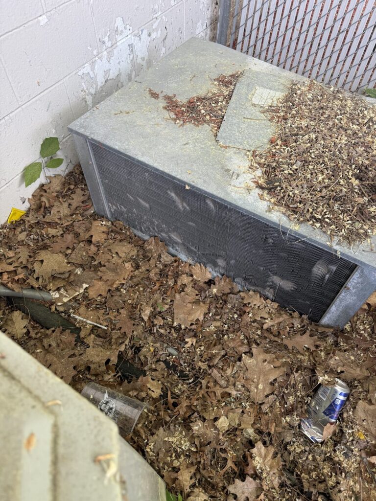 Outdoor condensing unit buried in fallen leaves against building wall