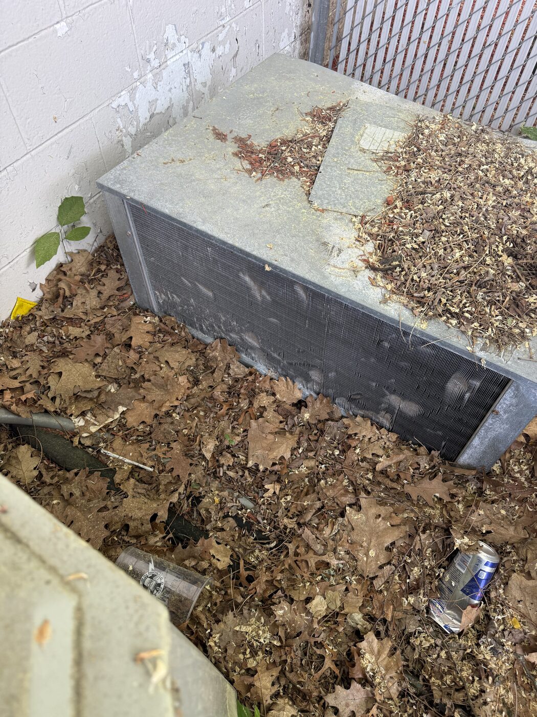 Outdoor condensing unit buried in fallen leaves against building wall