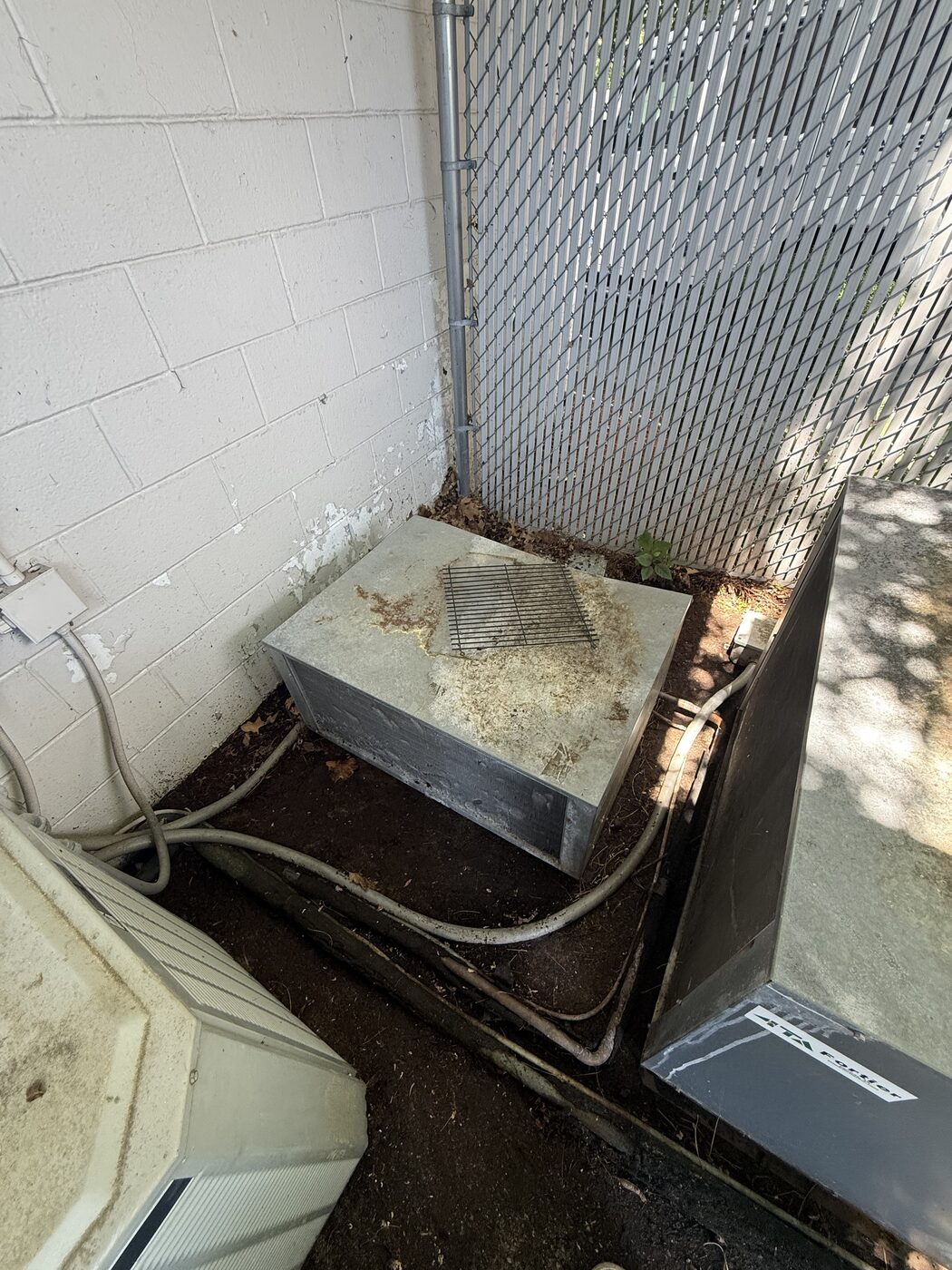 Outdoor refrigeration condensing unit on a concrete pad against a fenced exterior wall