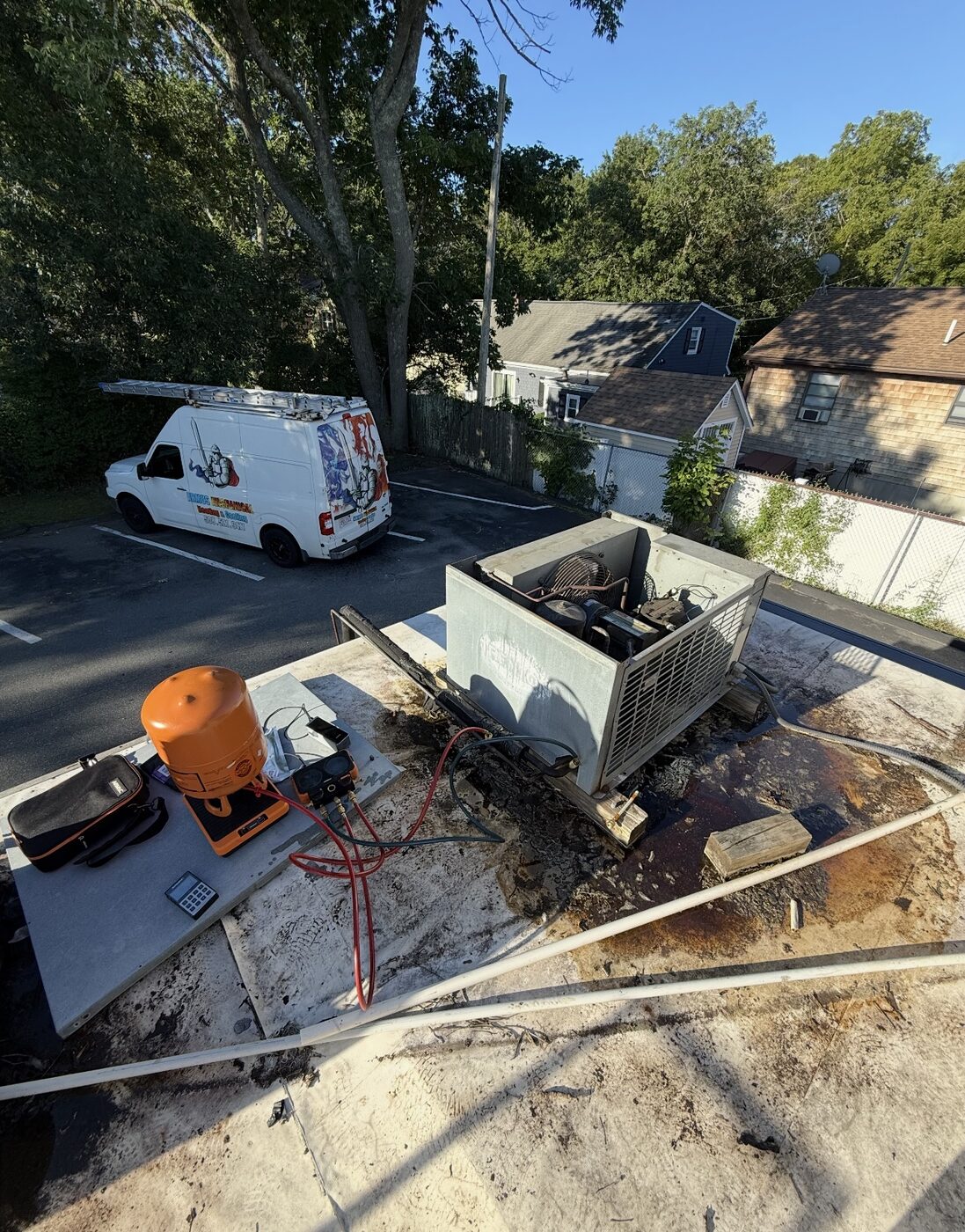Rooftop refrigeration condensing unit being serviced with gauges and a service van below