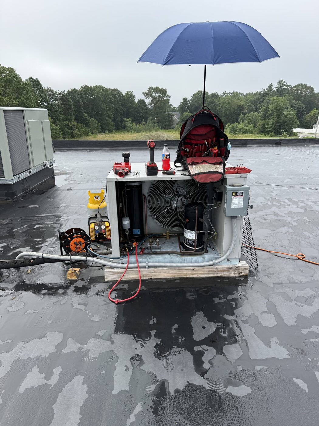 Rooftop refrigeration condensing unit being serviced in the rain under an umbrella
