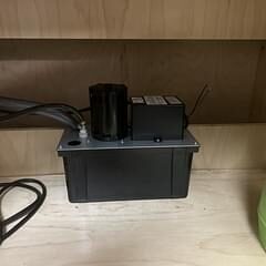 Black condensate removal pump with reservoir and drain tubing installed under a wooden counter