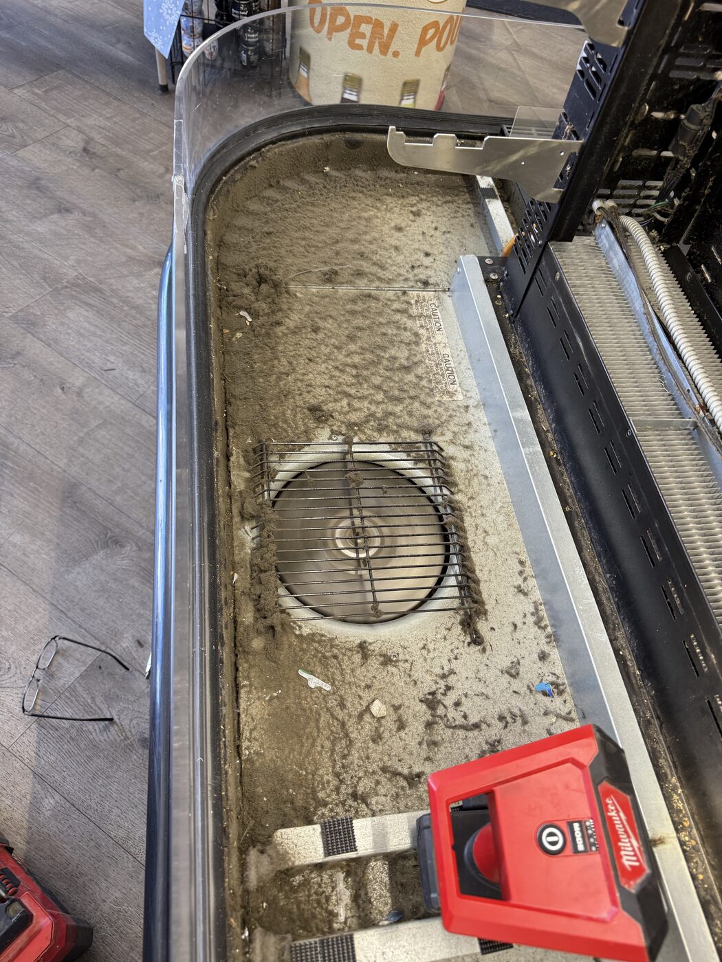 Dirty drain pan and evaporator fan grille inside a curved deli display case during cleaning