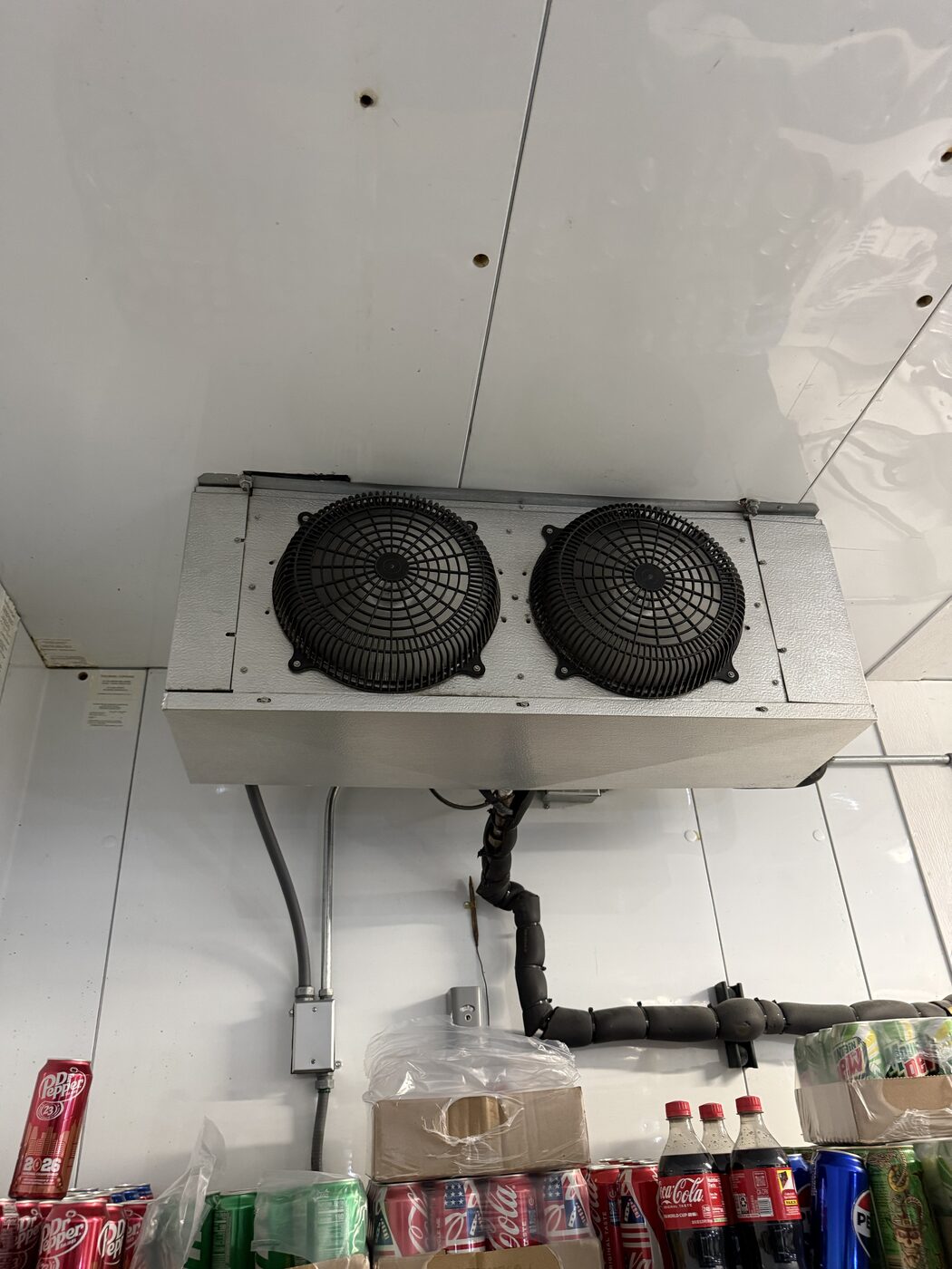 Dual-fan walk-in cooler evaporator unit mounted on the ceiling above stocked beverage shelves