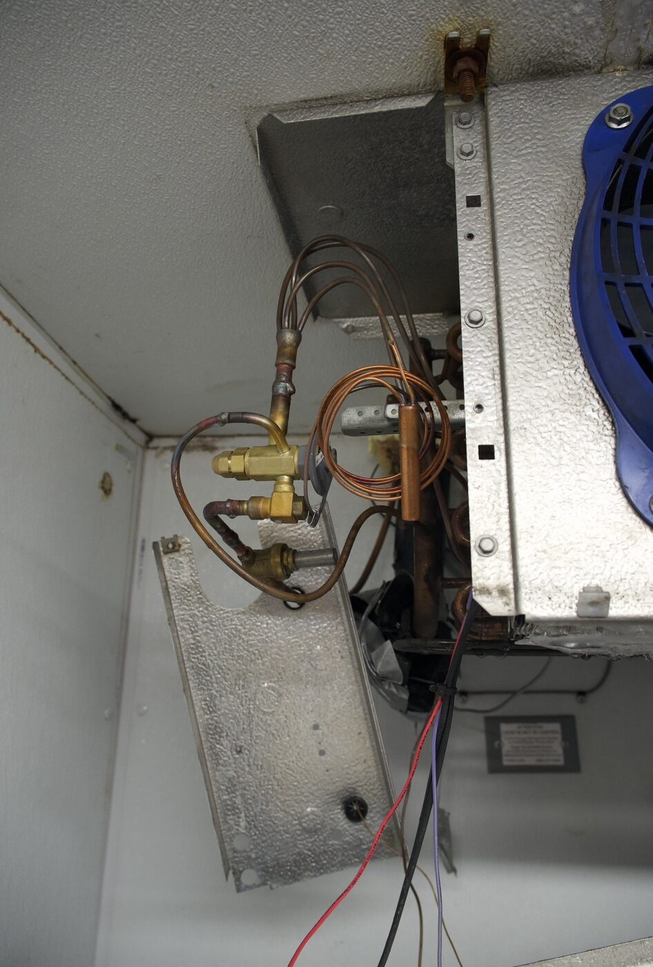 Close-up of a walk-in evaporator unit showing copper lines, TXV expansion valve and capillary tube