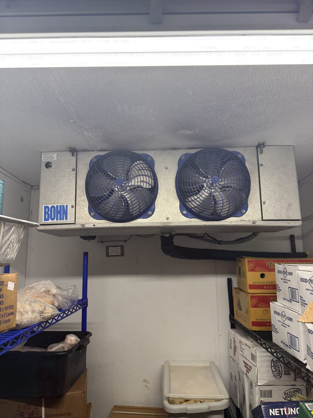 Bohn two-fan walk-in cooler evaporator coil mounted on the ceiling of a stocked walk-in